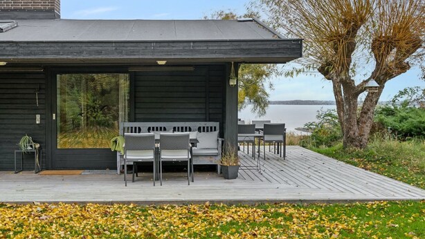 Una casa moderna con una terraza, asientos al aire libre y vista al agua.