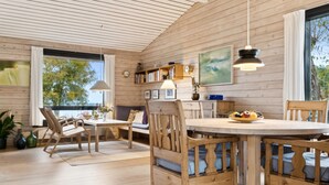 Un interior de madera con una zona de comedor, estanterías y un amplio ventanal con vistas a árboles.