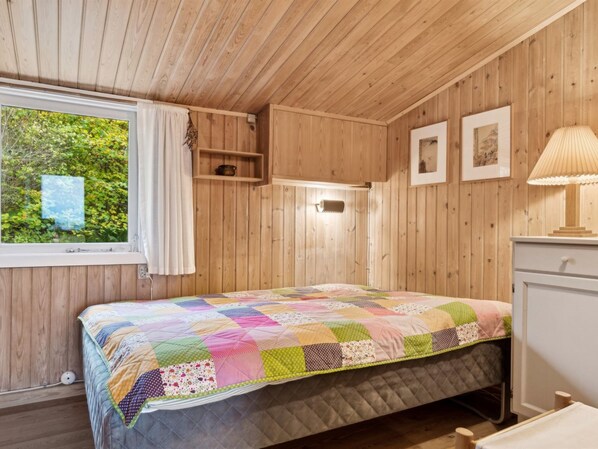 A cozy bedroom with a quilted bed, wooden walls, a window with a view of greenery, and a bedside table with a lamp. - "Adelbert" - 600m to the fjord by Interhome (Jægerspris)