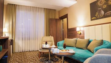 A hotel room with a teal sofa, a wooden headboard, a dining table with a teapot and cups, and a patterned carpet.