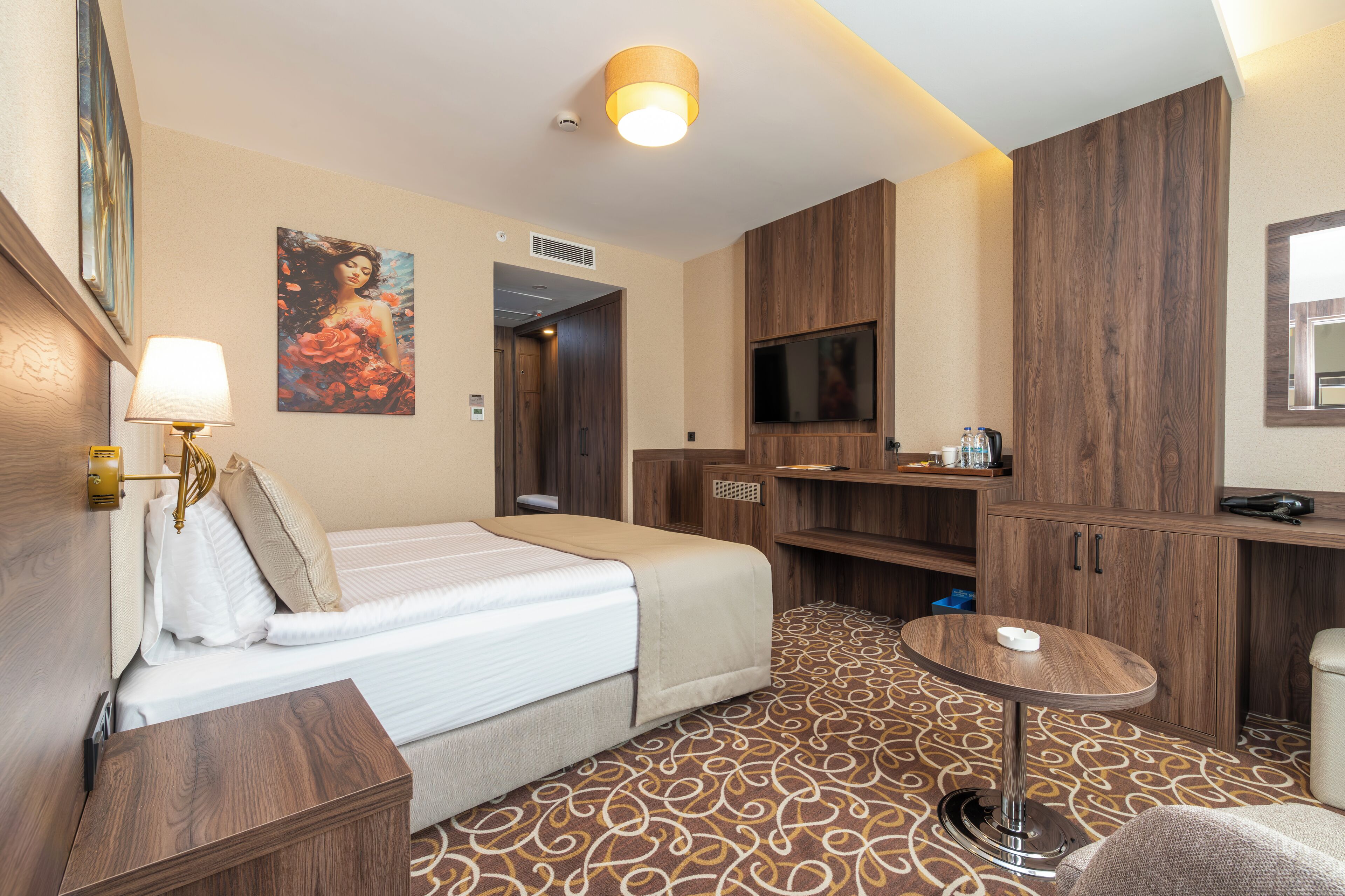 Una habitación de hotel con una cama, una mesita, un televisor y armarios de madera.