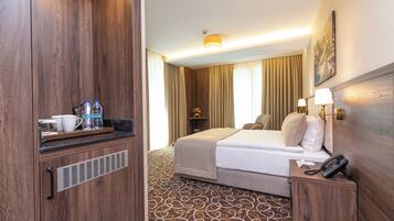 Habitación de hotel con una cama, mesita de noche con un teléfono, una pequeña mesa con botellas de agua, una taza y una bandeja.