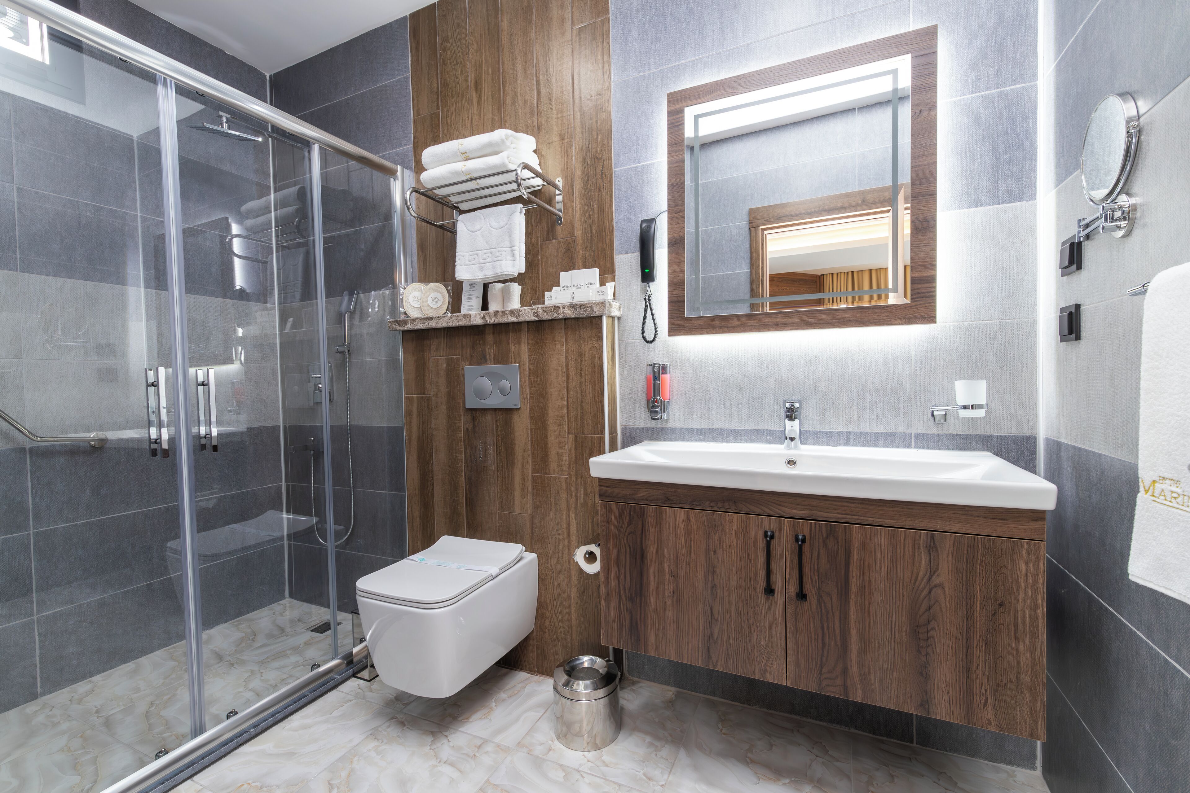 Un baño moderno con cabina de ducha de vidrio, inodoro blanco, lavabo con tocador de madera y espejo sobre el lavabo.