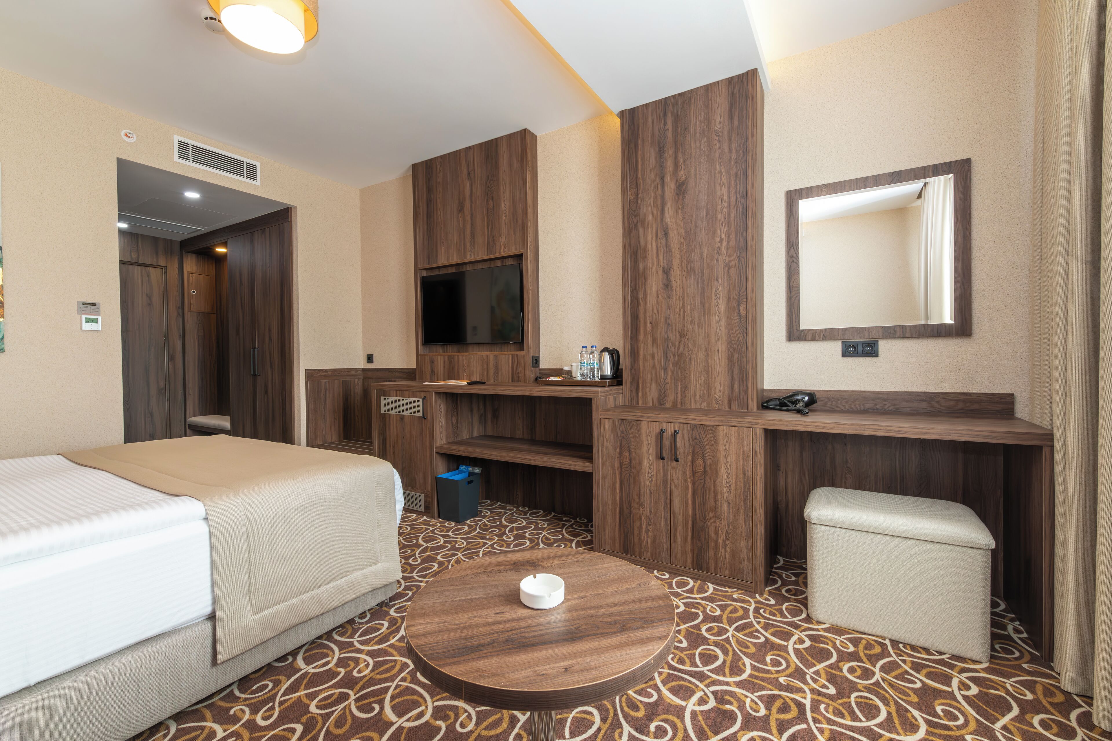 A hotel room with a bed, a small round table, a TV, a mirror, and a wardrobe.