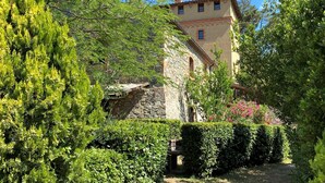 A stone building with a tiled roof, surrounded by lush greenery and a clear blue sky.