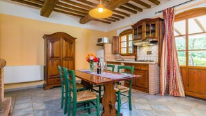A dining area with a wooden table and chairs, a vase with flowers, and a kitchen in the background. - Apartment Talpa by Interhome (Riparbella)