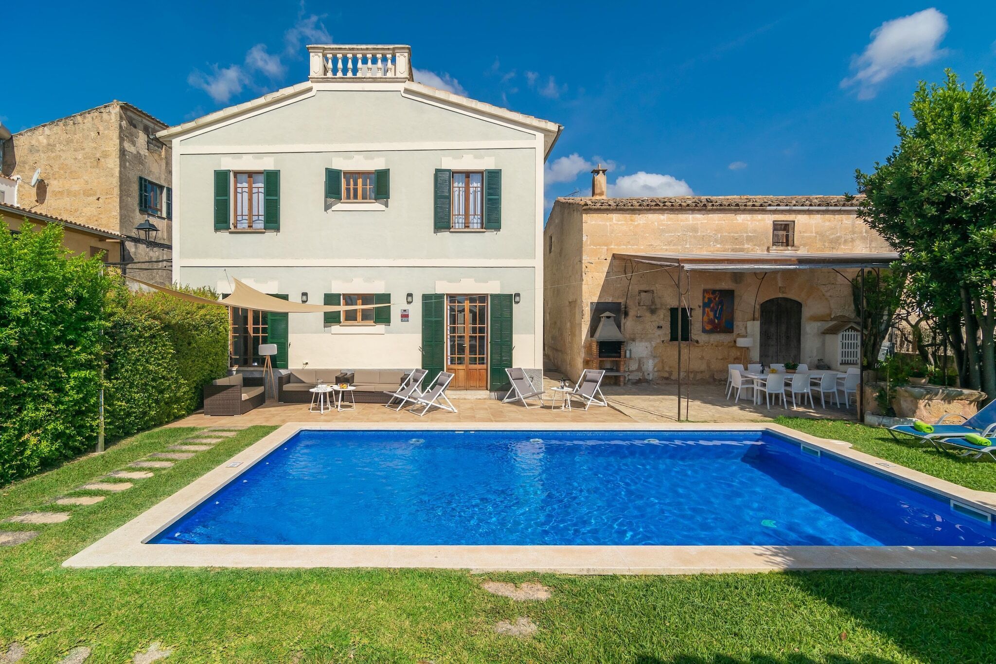 A two-story building with a swimming pool, outdoor seating, and a garden.