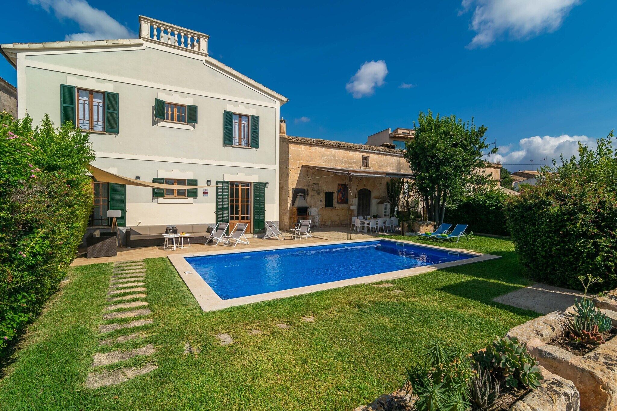 A two-story house with a swimming pool, green shutters, and outdoor seating.