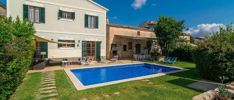 A two-story house with a swimming pool, green shutters, and outdoor seating.