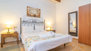 Een net opgemaakt bed met een bloemenprint, twee bedlampjes, een houten nachtkastje, een grote spiegel en een houten garderobe.