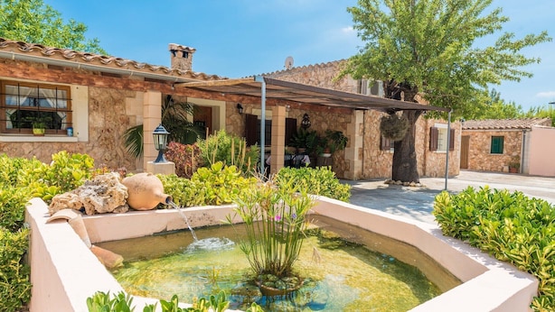 A courtyard with a fountain, surrounded by lush greenery and a stone building with a tiled roof. - Can Tomeu - Villa With Private Pool In Inca (Inca, Illes Balears)