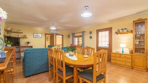 A dining area with a wooden table and chairs, a sofa, and a kitchen in the background. - Can Tomeu - Villa With Private Pool In Inca (Inca, Illes Balears)