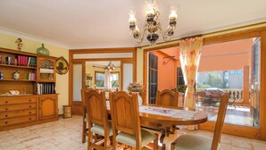 A dining area with a wooden table and chairs, a chandelier, and a view of the outside.