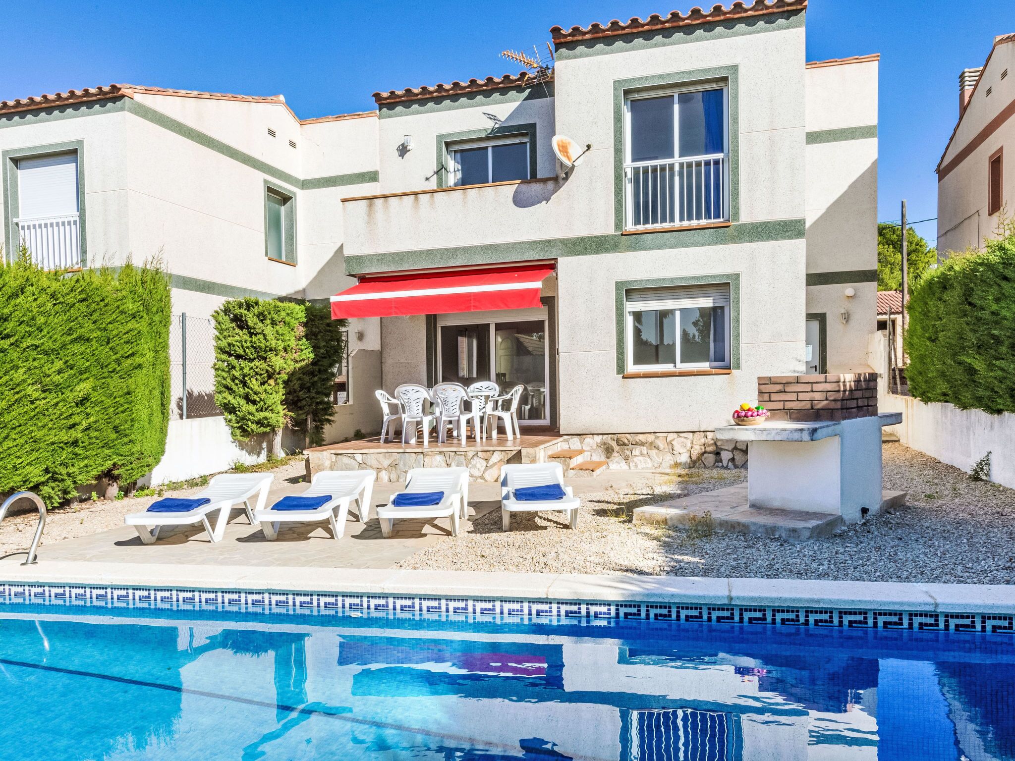 A two-story house with a swimming pool, outdoor seating, and a red awning.