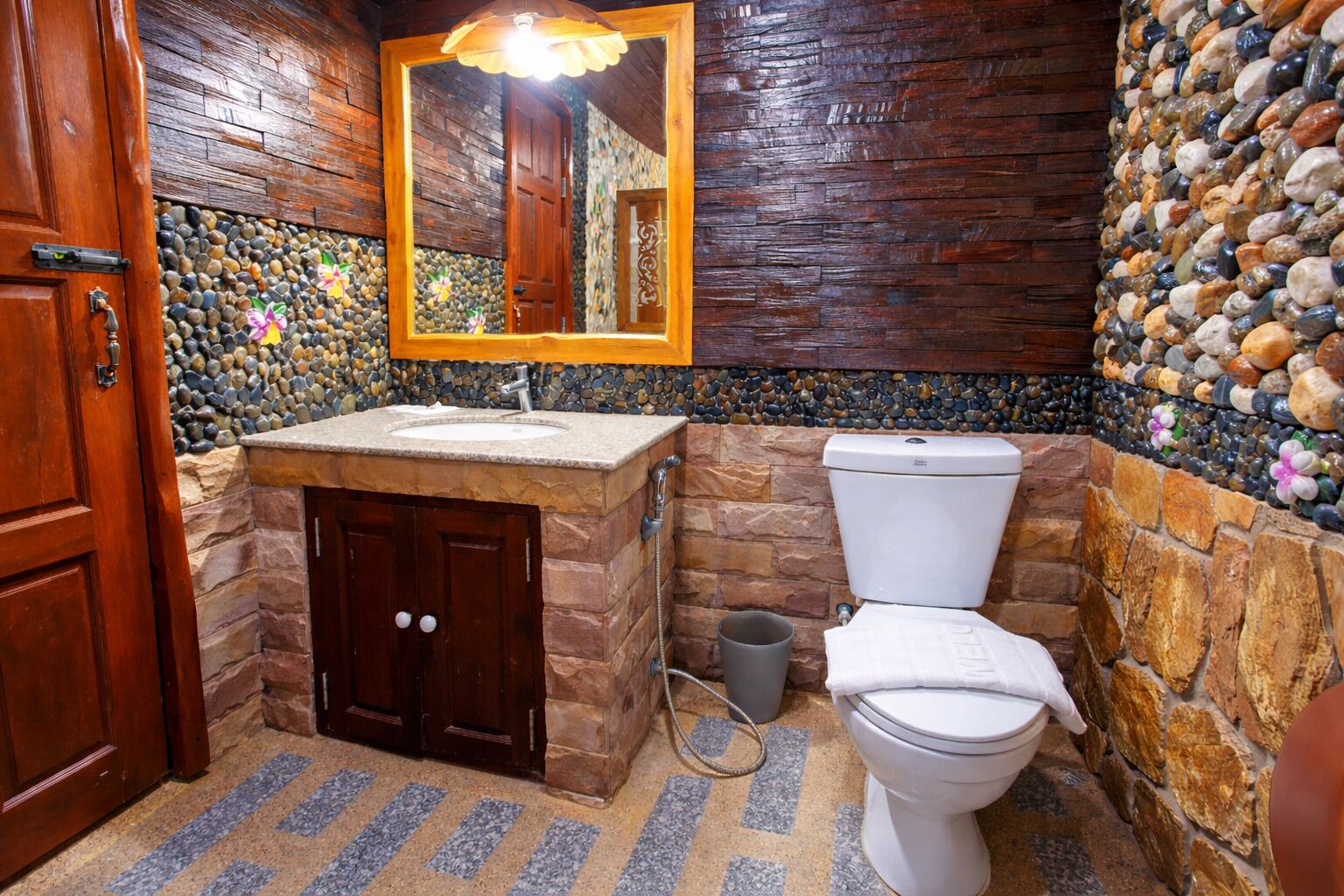Une salle de bain avec une porte en bois, un lavabo en pierre, des toilettes et un miroir avec un cadre en bois.