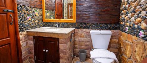 Un baño con puerta de madera, lavamanos de piedra, inodoro y espejo con marco de madera.