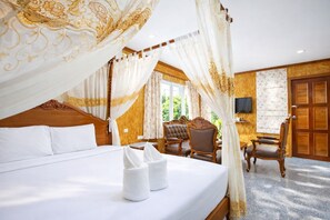 A bedroom with a four-poster bed, a sitting area with a chair and a table, and a television on the wall. - Chatsuree Boutique Resort (Ubon Ratchathani)