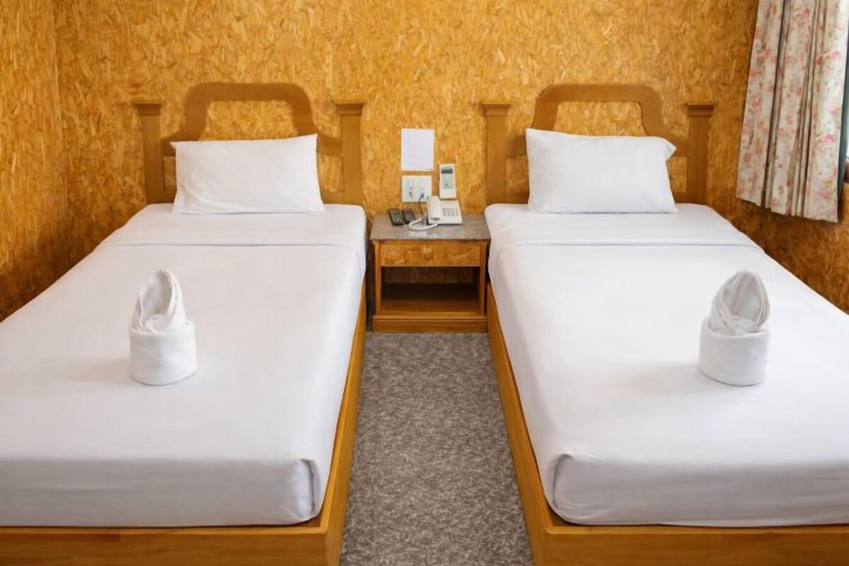 Ein Doppelzimmer mit zwei Betten, Holz-Kopfteilen, weißen Bettwäsche und einem Teppichboden. Ein kleiner Nachttisch mit Telefon ist ebenfalls vorhanden.