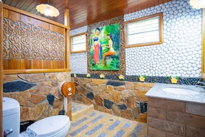 A bathroom with a stone wall, a wooden panel, a painting, and a sink. - Chatsuree Boutique Resort (Ubon Ratchathani)
