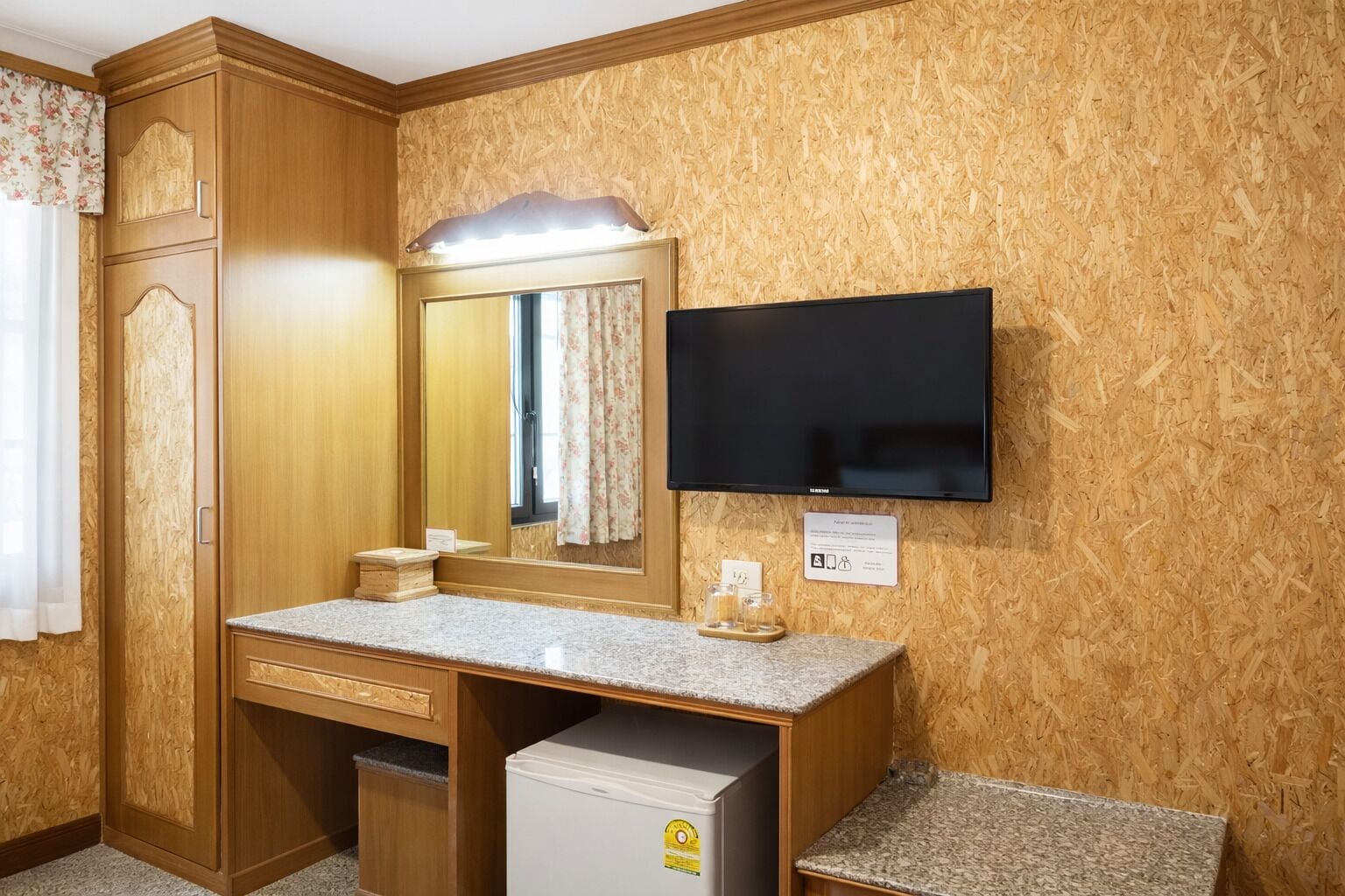 Ein Hotelzimmer mit einem Holzschrank, einem Frisiertisch mit Spiegel, einem an der Wand montierten Fernseher und einem kleinen Kühlschrank.