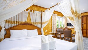 A four-poster bed with a canopy, a wooden headboard, a television on a stand, and a seating area with a chair and a table. - Chatsuree Boutique Resort (Ubon Ratchathani)