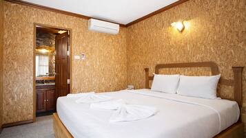 A hotel room with a wooden wall, a bed with white linens, a wooden headboard, and an air conditioning unit.
