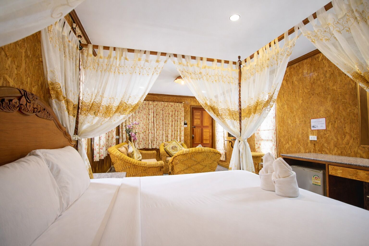 Quarto de hotel com cama, área de estar com mobiliário de vime e uma mesa de trabalho.