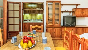 A dining area with a wooden table set for a meal, a fruit platter, and a television on a wooden cabinet.