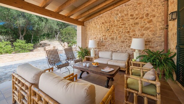 Un espace extérieur aménag é, abrité et doté de mobilier en osier, de murs en pierre et offrant une vue sur le paysage environnant.