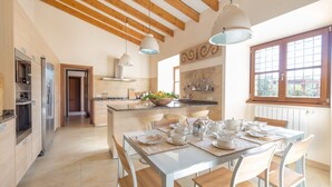 Une cuisine moderne avec des poutres en bois, un coin repas avec une table dressée pour quatre personnes, et une vue par la fenêtre.