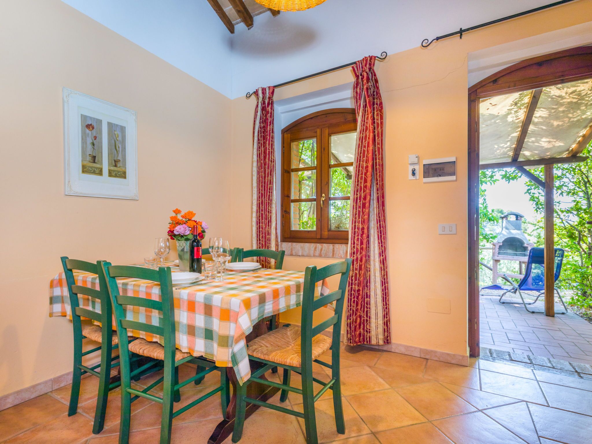 A dining area with a table set for four, green chairs, a checkered tablecloth, and a window with curtains.