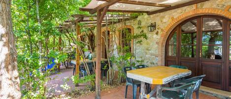 An outdoor patio with a wooden pergola, stone walls, and a table with chairs.