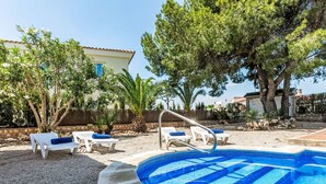 A swimming pool with blue tiles, surrounded by white lounge chairs with blue cushions, and trees.