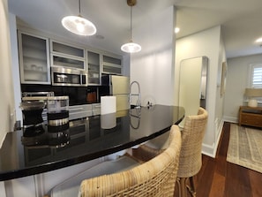 A modern kitchen with a black countertop, stainless steel appliances, and wicker chairs.