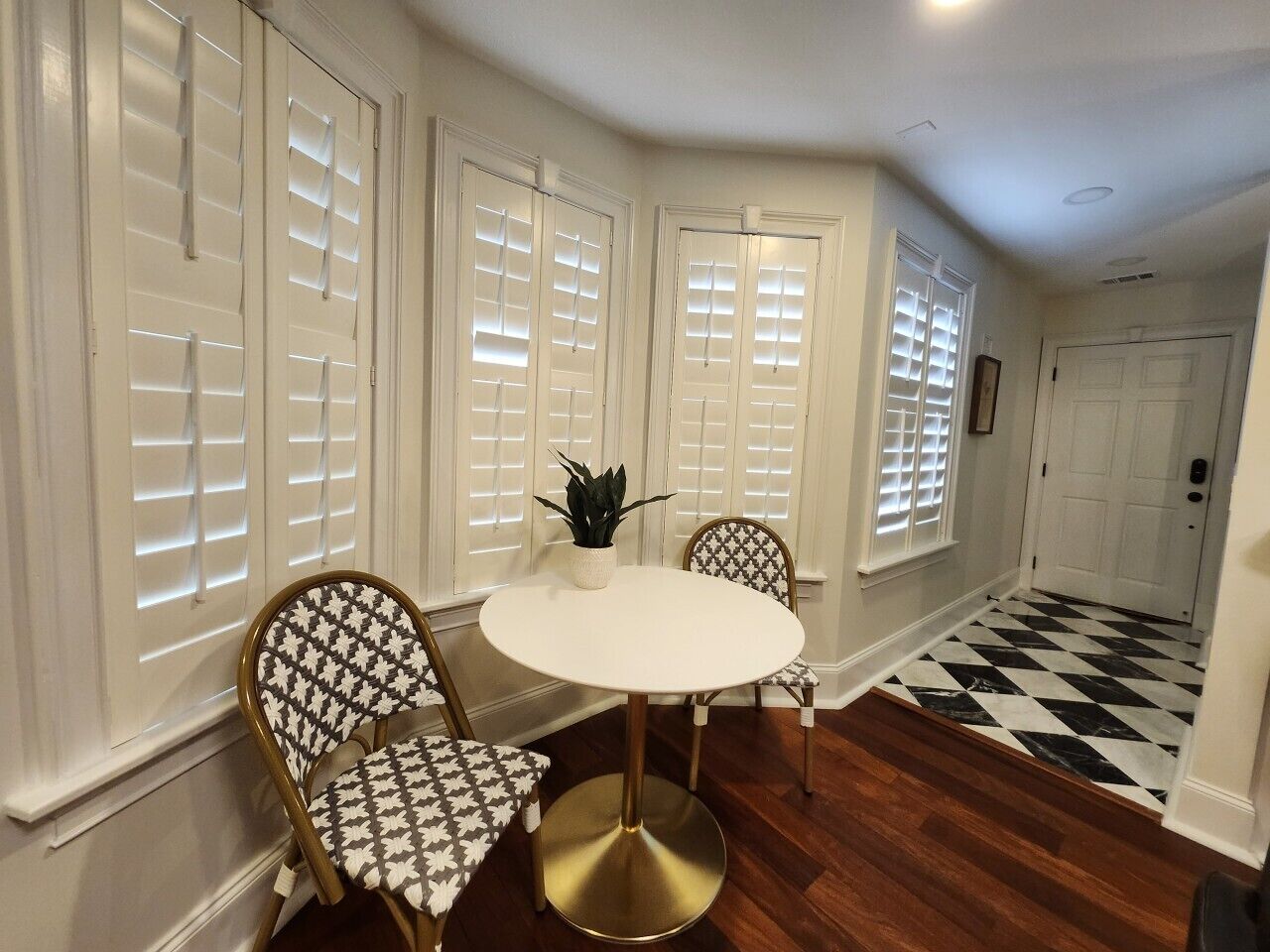 A dining area with a round table and chairs, a potted plant, and a checkered floor.