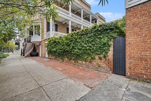 A residential street with a brick house, a covered porch, and a hedge. - Carriage House B at the Hamilton House (Savannah)