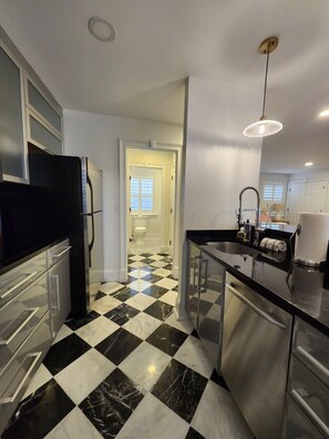 A kitchen with a black and white checkered floor, a stainless steel refrigerator, and a modern pendant light. - Carriage House B at the Hamilton House (Savannah)