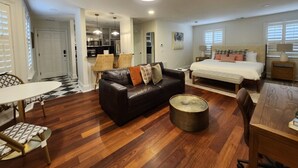 A modern living room with a leather sofa, a round coffee table, a dining area with a table and chairs, a bedroom with a bed and nightstands, and a kitchen area. - Carriage House B at the Hamilton House (Savannah)