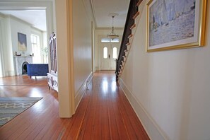 A hallway with wooden floors, a blue chair, a staircase with a railing, and a painting on the wall. - Hamilton House - 5 Bed Historic Downtown House w/ Courtyard & Parking (Savannah)