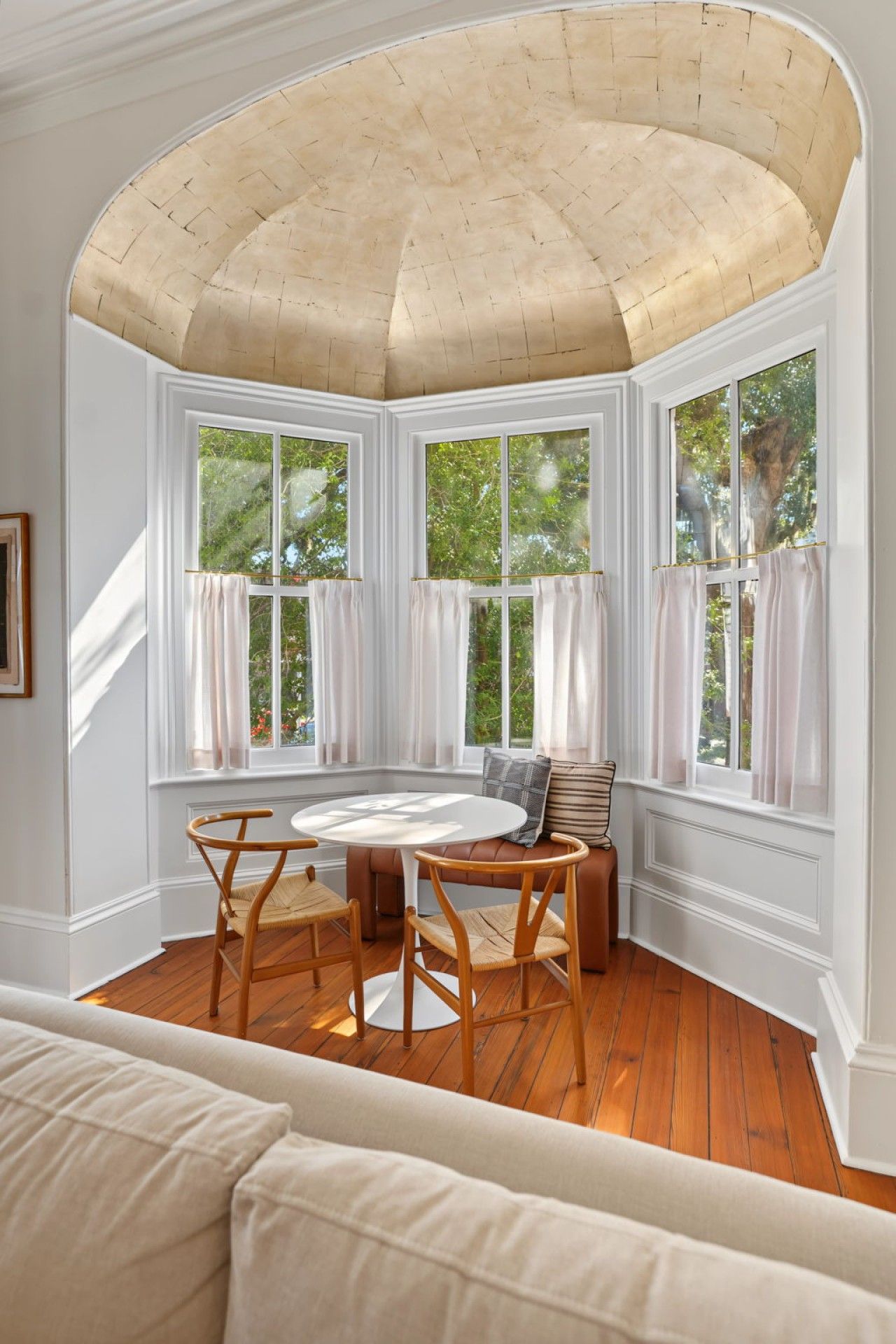 Una habitación con una mesa redonda, sillas de madera, un banco y vistas amplias a través de ventanas grandes.