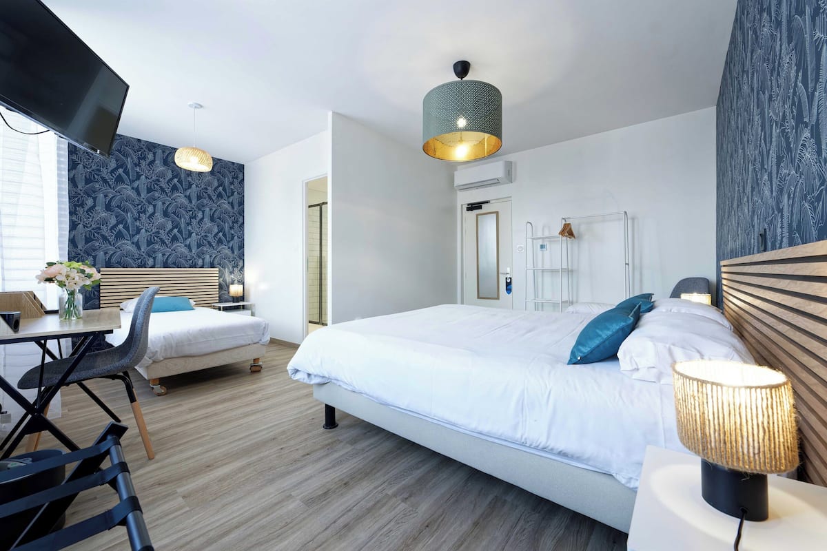A modern hotel room with a large bed, a desk with a chair, a TV, and a decorative lamp.