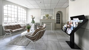 A spacious lobby with a large arched window, a fireplace, and a display of brochures. - Hôtel le Terminus et son restaurant Côte à Côte (Autun)