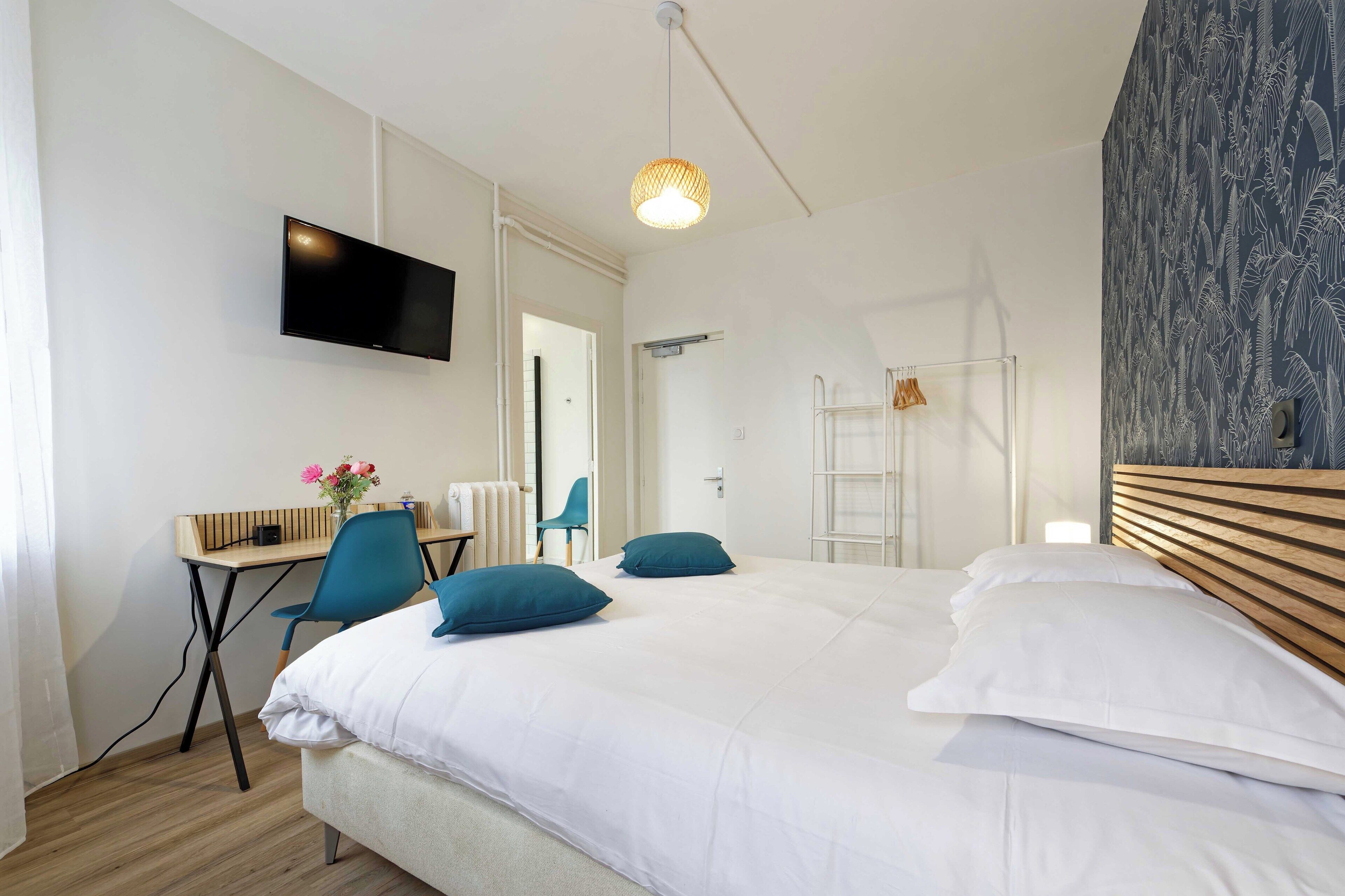 A modern hotel room with a large bed, a desk with a chair, a television, and a shower area.