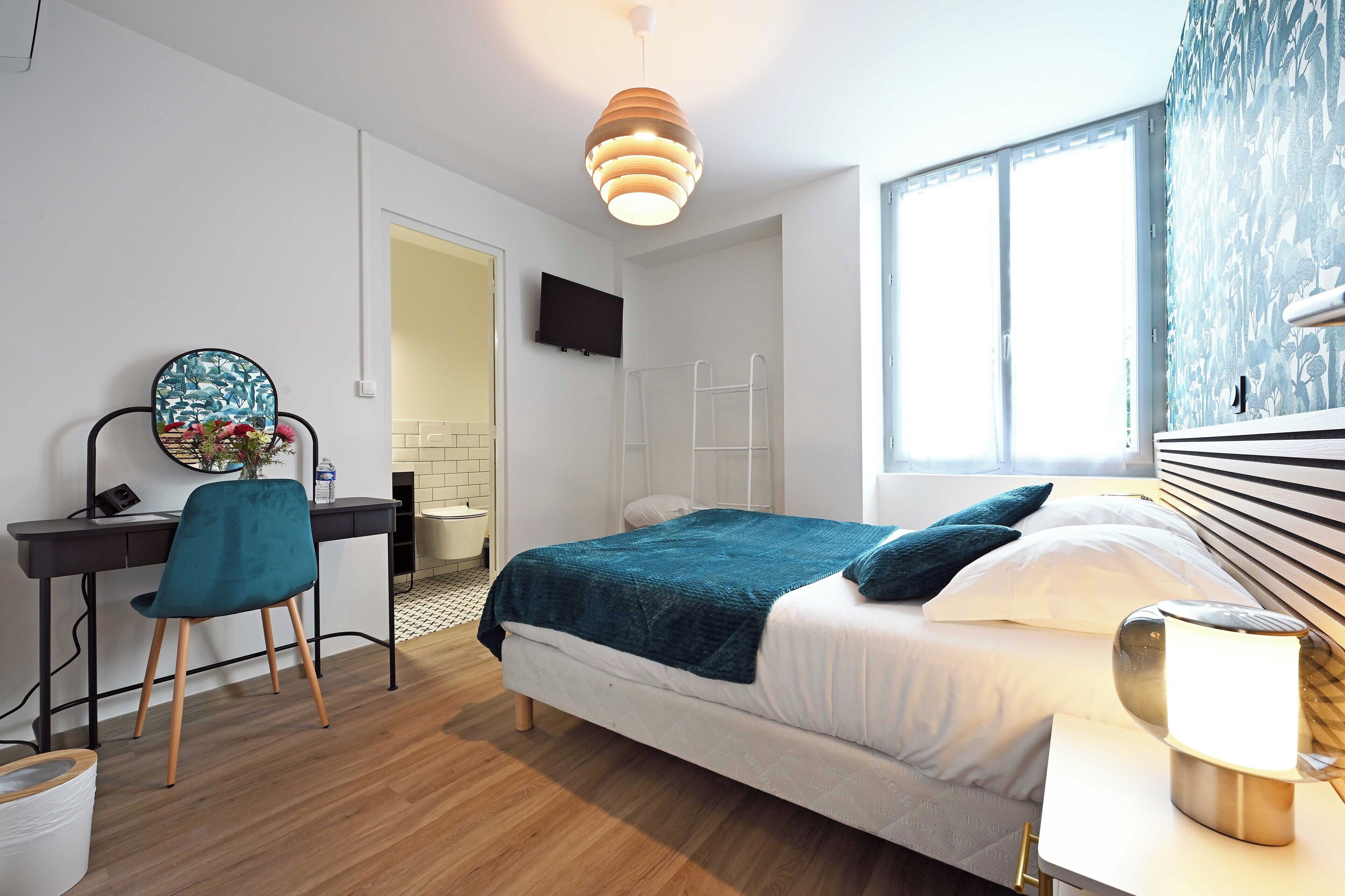 A modern bedroom with a bed, desk, chair, and a TV.
