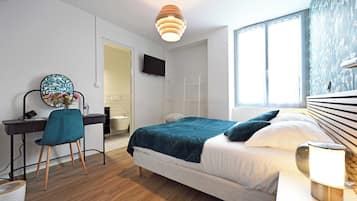 A modern bedroom with a bed, desk, chair, and a TV.