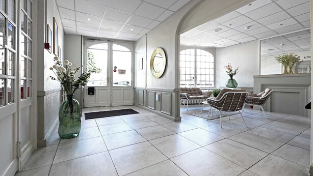 A spacious lobby with a tiled floor, a large mirror, and a seating area with wicker chairs. - Hôtel le Terminus et son restaurant Côte à Côte (Autun)