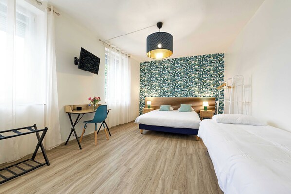 Ein Hotelzimmer mit einem Bett, einem Schreibtisch, einem Sessel sowie einem Fernseher und einer Wand mit Muster.