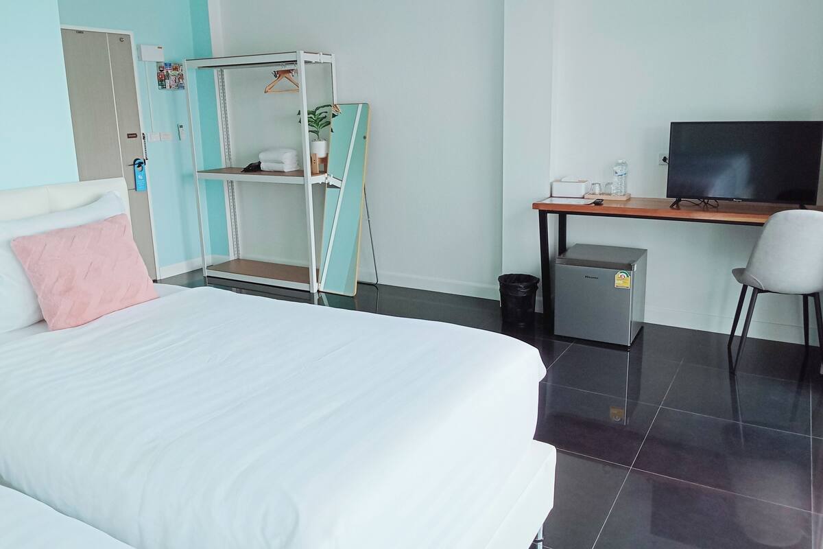 Ein Hotelzimmer mit einem Bett, einem Schreibtisch mit Computer, einem Fernseher, einer kleinen Kühlbox und einem Papierkorb.