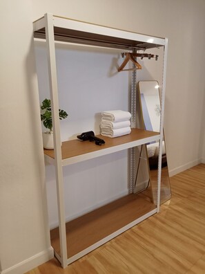 Un vestidor con espejo, repisas con toallas dobladas, una planta en maceta y un perchero.