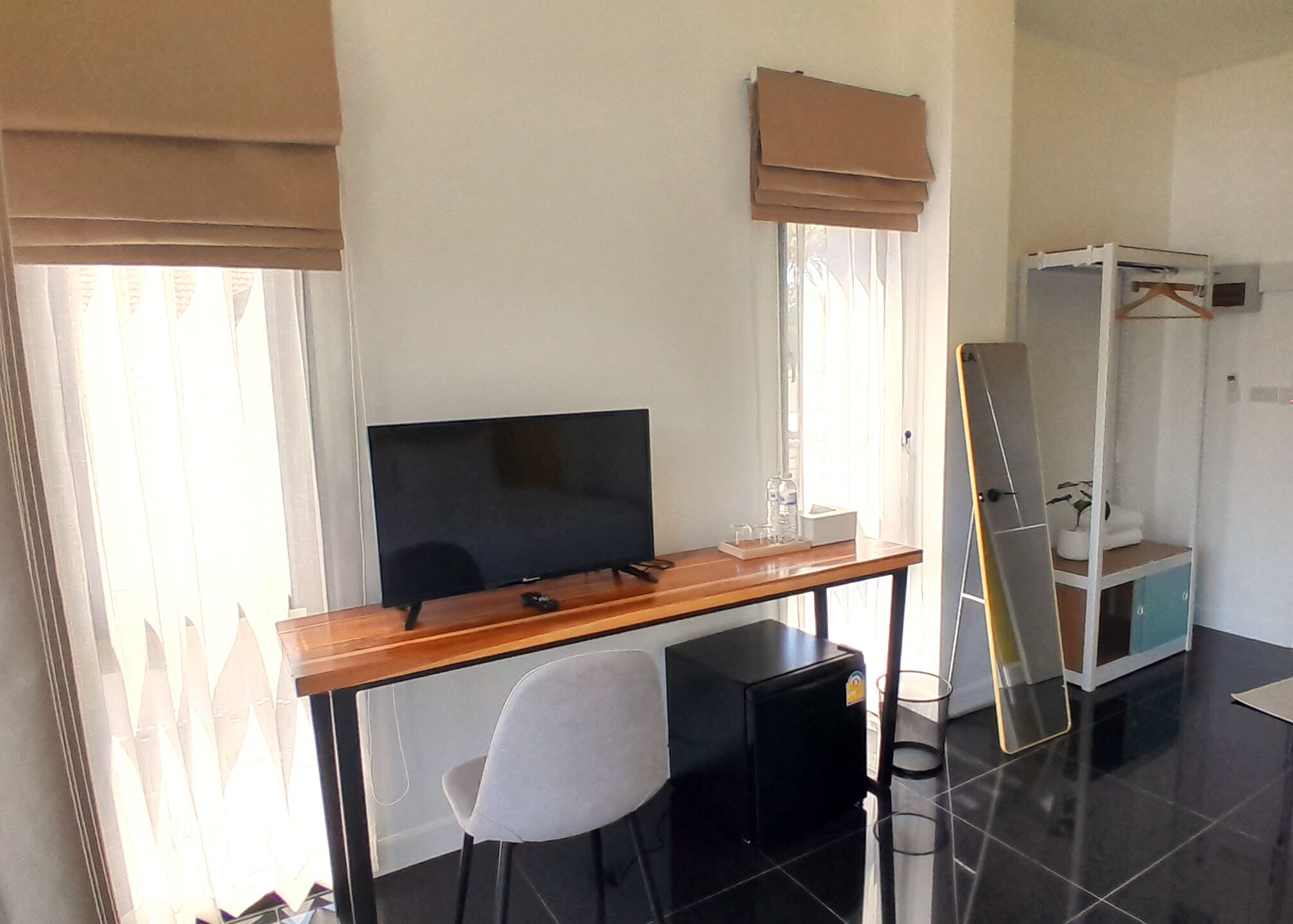 Habitación de hotel compacta con escritorio de madera, televisor, silla, armario y espejo.